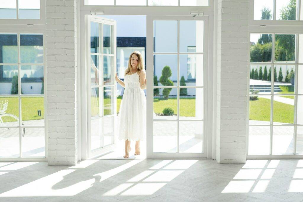 Elegant woman enters the open door of a house with high panoramic windows