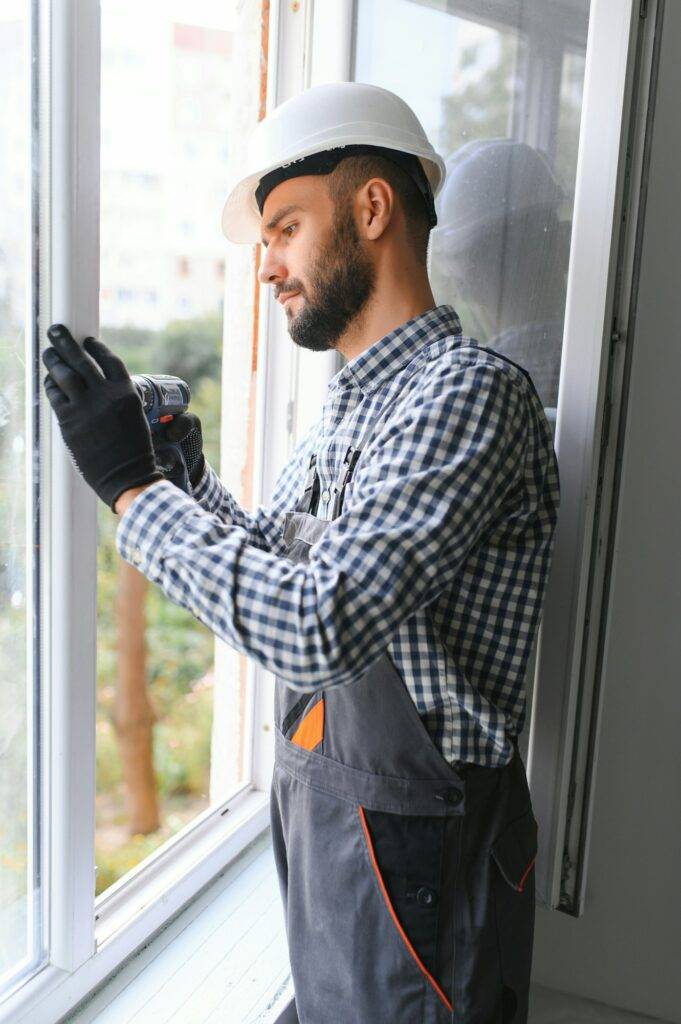 Workman in overalls installing or adjusting plastic windows in the living room at home